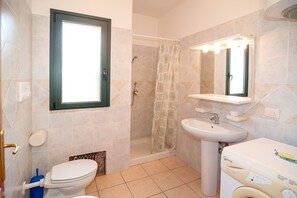 A bathroom with a toilet, sink, shower, and a window.