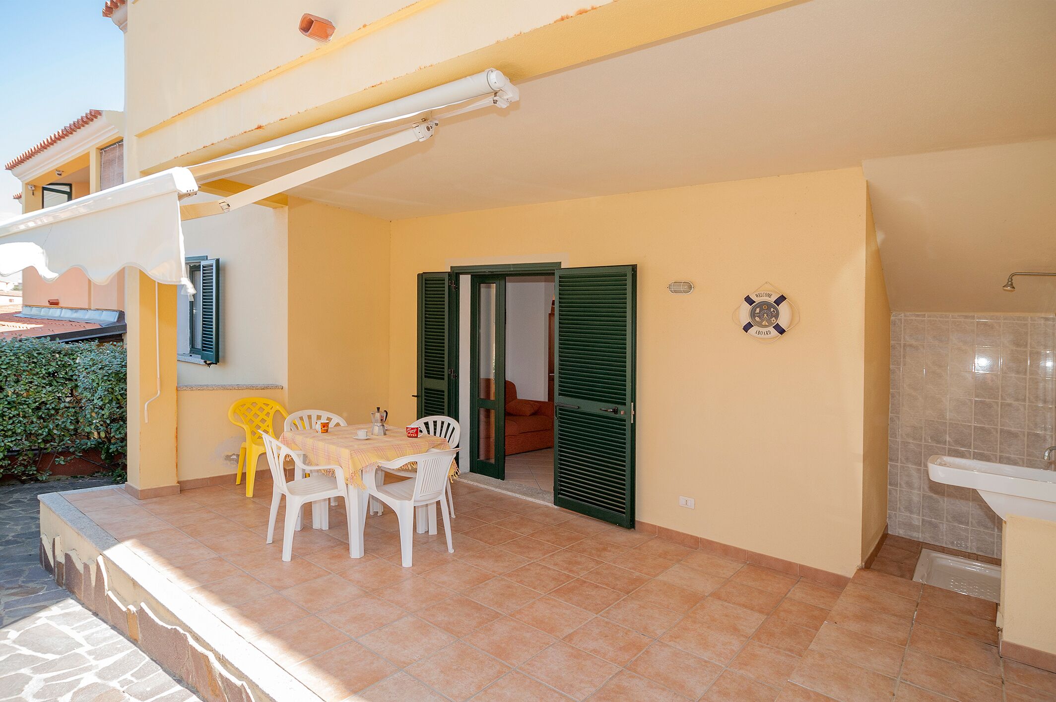 A covered outdoor patio with a table and chairs, a door leading to a room, and a tiled bathroom area.