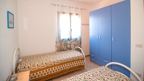 Une chambre à coucher comprenant un lit, un bureau, une chaise, une armoire et une fenêtre avec des rideaux.