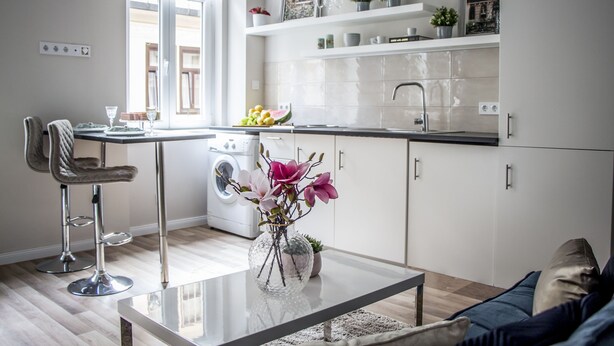 Ett modernt kök med tvättmaskin, en matplats med ett glasbord och ett vardagsrum med en soffa.