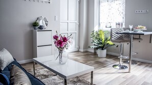 Ett modernt vardagsrum med ett vitt soffbord, en soffa, en matplats med barstolar och en krukväxt.