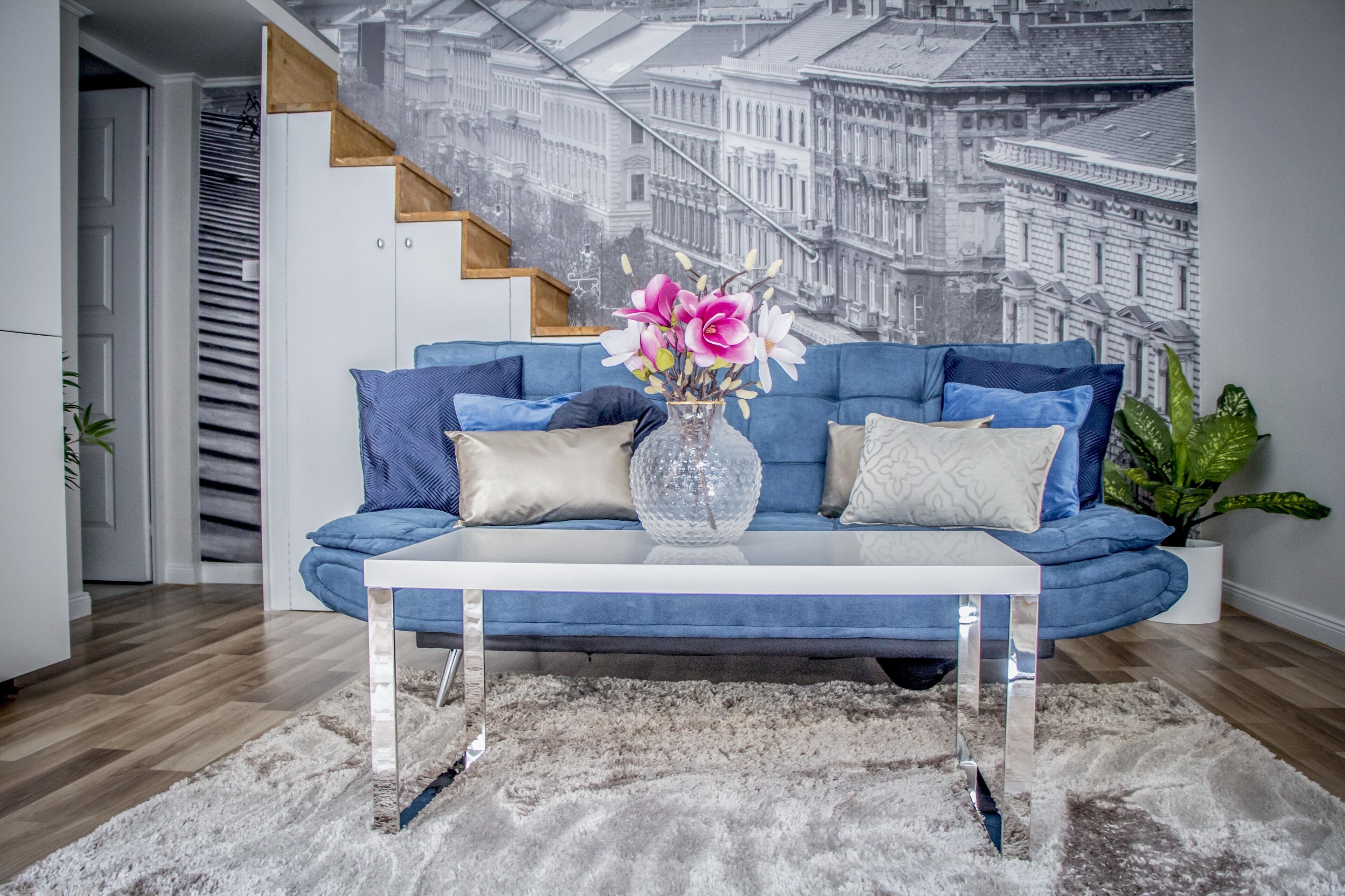 Ein modernes Wohnzimmer mit einem blauen Sofa, einem Glastisch und einer dekorativen Vase mit Blumen.