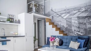 Ett modernt vardagsrum med kök, en blå soffa och en väggmålning som föreställer en stadsbild.