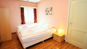 Ein Schlafzimmer mit Bett, Nachttisch mit Lampe, Fenster mit Vorhängen und einer Tür.