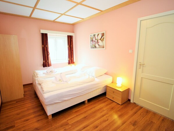 A bedroom with a bed, a bedside table with a lamp, a window with curtains, and a door. - Apartment in St. Michael near Ski Slopes (Sankt Michael im Lungau)