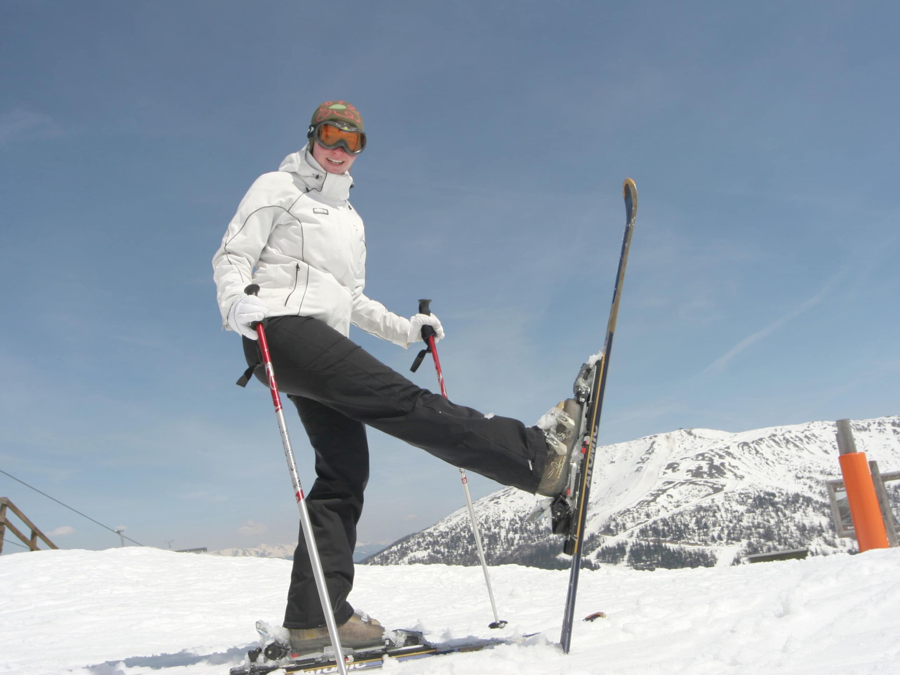 Eine Person fährt auf einem verschneiten Hang, am Himmel ist es klar und im Hintergrund sind Berge zu sehen.
