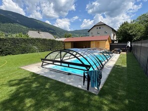 A swimming pool with a glass enclosure, a house in the background, and a hilly landscape. - Apartment in St. Michael near Ski Slopes (Sankt Michael im Lungau)