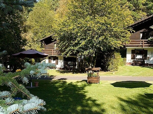 A lodge with a covered patio, a wooden deck, and a well-maintained lawn. - Feriendorf Reinskopf in der Eifel (Schoenecken)