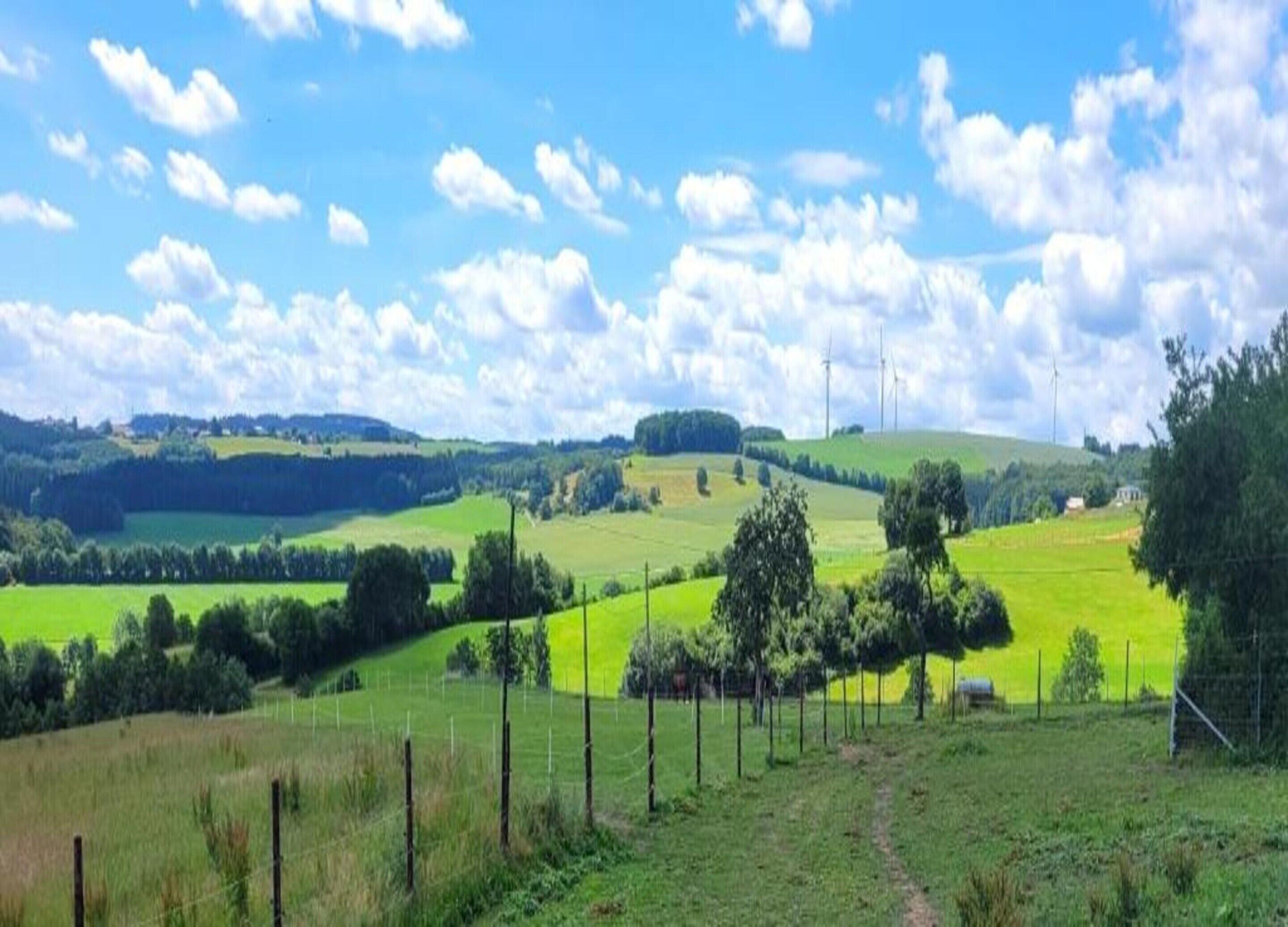 A rural landscape with rolling hills, green fields, and a clear sky.