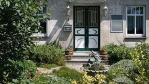 A house with a green door, two windows, and a garden with various plants and flowers. - Comfy Apartment in Kröpelin near Sea Beach (Kroepelin)