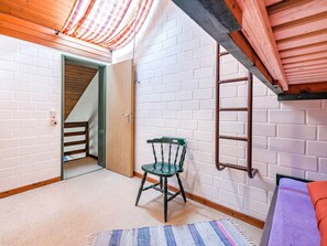 Cozy loft space with a wooden ladder, single chair, and plush sofa, offering a unique retreat.