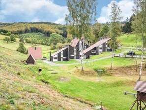 A rural setting with a row of wooden houses, a small barn, and a car parked on the road.