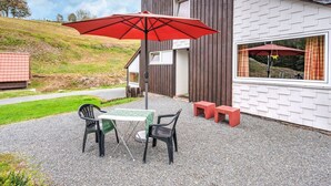 Un espace patio avec une table et des chaises, un parasol rouge et un bâtiment moderne doté d’une façade en bois.