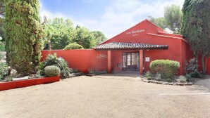 A red building with a sign 'Les Gardians' and 'Odalys' on the facade, surrounded by greenery and a gravel driveway. - Resort in Arles With Pools Near Camargue (Arles)