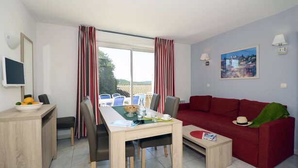 Ein modernes Wohnzimmer mit Essbereich, roten Vorhängen, einem roten Sofa, einem Fernseher und einem Gemälde an der Wand.