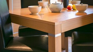 Een eettafel met stoelen, een televisie erboven, een vaas en een raam met uitzicht op een berg.