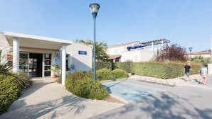 Entrada de hotel com galeria coberta, poste de luz e área de estacionamento.