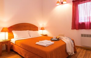 A neatly made bed with a wooden headboard, two bedside lamps, a tray with a cup and pastries, and a window with a red curtain. - Nature Retreat With Terrace (Vallon-Pont-d'Arc)