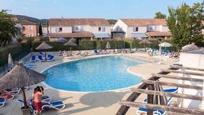 Uma piscina com espreguiçadeiras e guarda-sóis, rodeada por edifícios com telhados em cerâmica.
