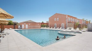 A swimming pool with lounge chairs and a building with a red facade. - Maisonette in Aigues-mortes Near Camargue (Aigues-Mortes)