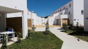 Un cortile con edifici bianchi, un tavolo di legno con sedie e piccole piante.