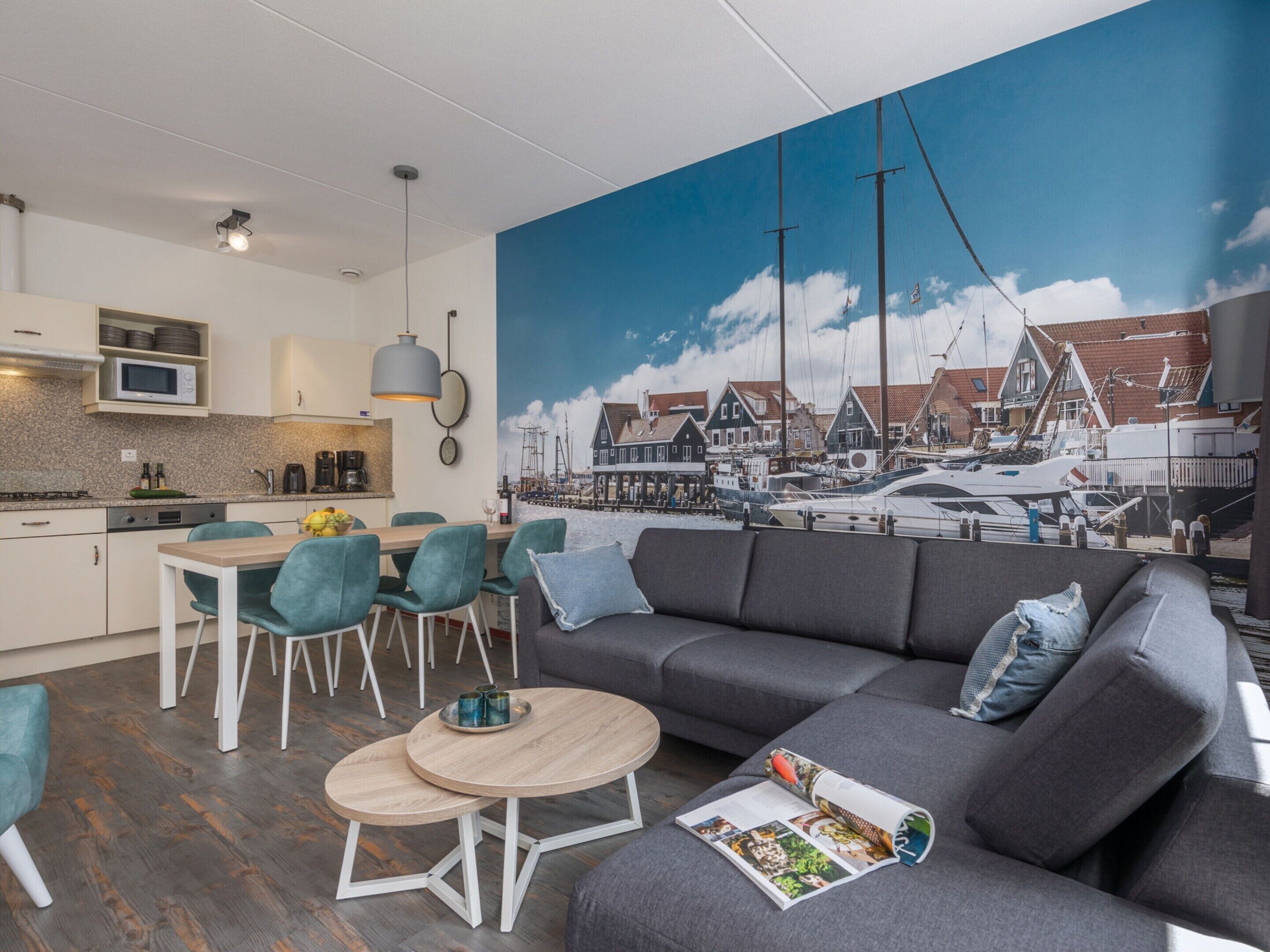 Una sala de estar moderna con un gran mural de temática náutica, un sofá gris, sillas color turquesa y una mesa de centro de madera.