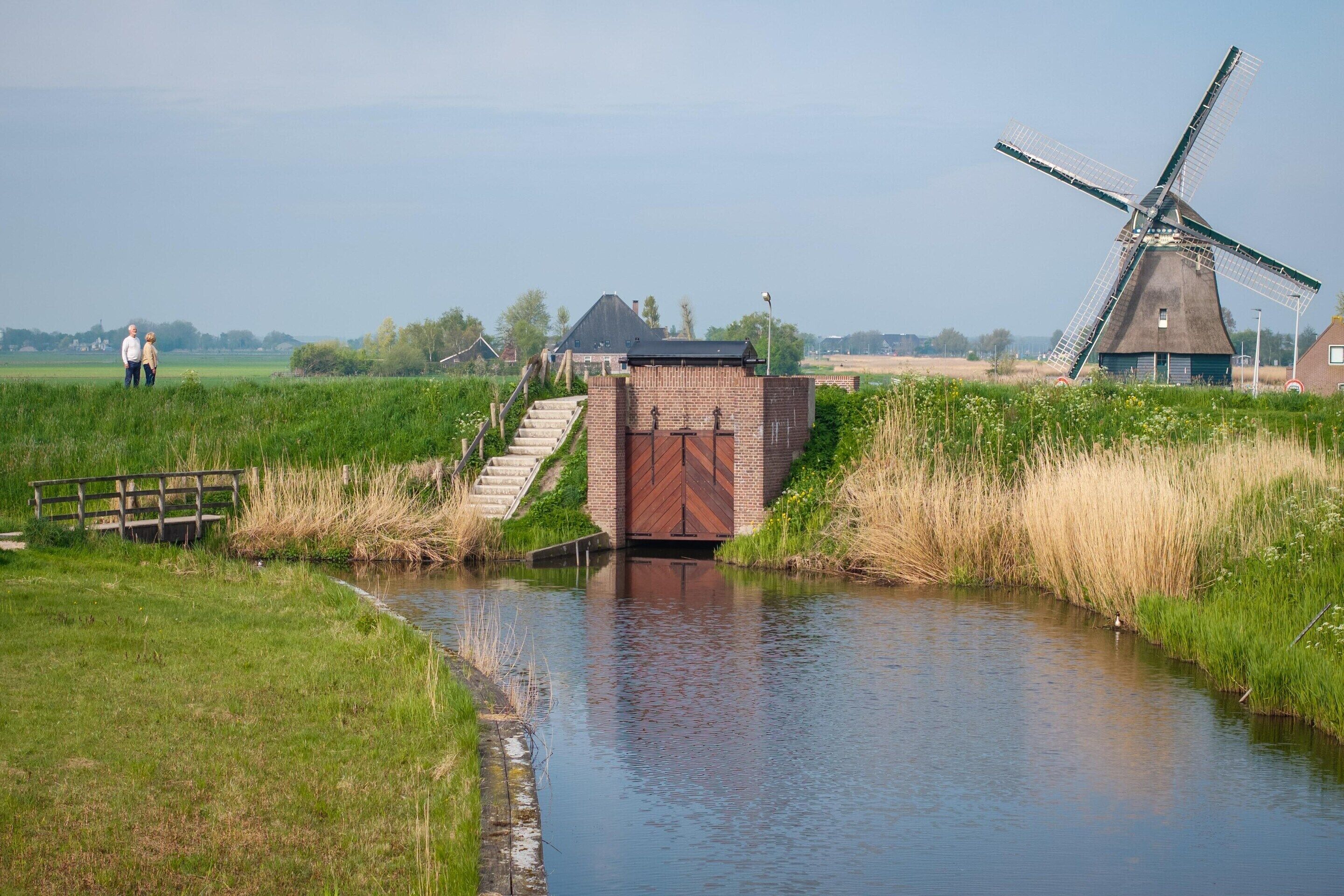 Een traditionele windmolen en een klein bakstenen gebouw aan een gracht.