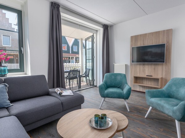 Uma sala de estar moderna com um sofá cinzento, poltronas verde-turquesa, uma mesa de centro redonda e uma TV fixada numa parede de madeira.
