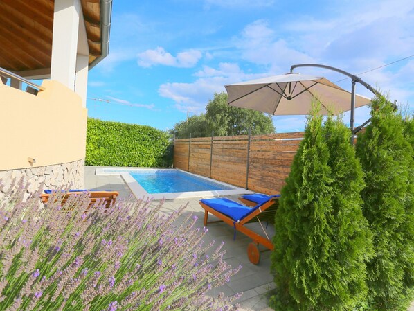A backyard with a swimming pool, lounge chairs, and a wooden fence.