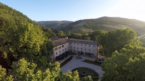 A large, white building with a central courtyard, surrounded by lush greenery and hills in the background.