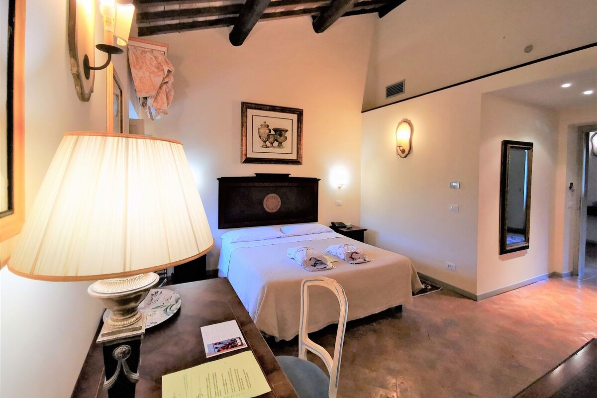 Une chambre d’hôtel avec un lit, une lampe de chevet, un tableau encadré et un bureau avec une lampe et des papiers.