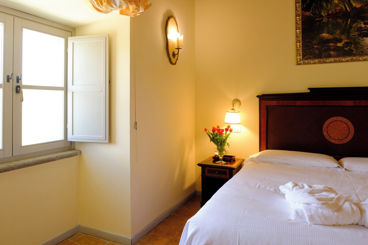 Hotelkamer met een bed, nachtkastje met een lamp, vaas met bloemen en een schilderij aan de muur.