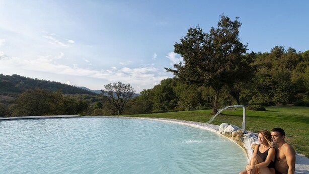 A couple sitting by a pool with a view of a green landscape and hills.