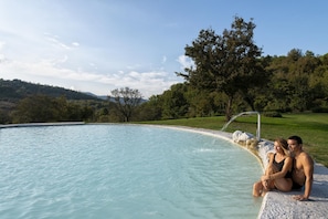 A couple sitting by a pool with a view of a green landscape and hills. - Hotel Terme di Stigliano (Canale Monterano)