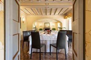 A dining area with a round table set for six, flanked by black chairs, under a coffered ceiling with wall sconces and a fireplace. - Hotel Terme di Stigliano (Canale Monterano)