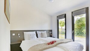 Una camera da letto moderna con un letto grande, una testiera con interruttore della luce e vista su un giardino tramite una porta scorrevole.
