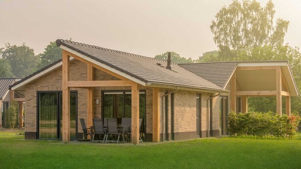 Ein modernes Haus mit Ziegelaußenwand, großen Fenstern und einer überdachten Terrasse mit Gartenmöbeln.