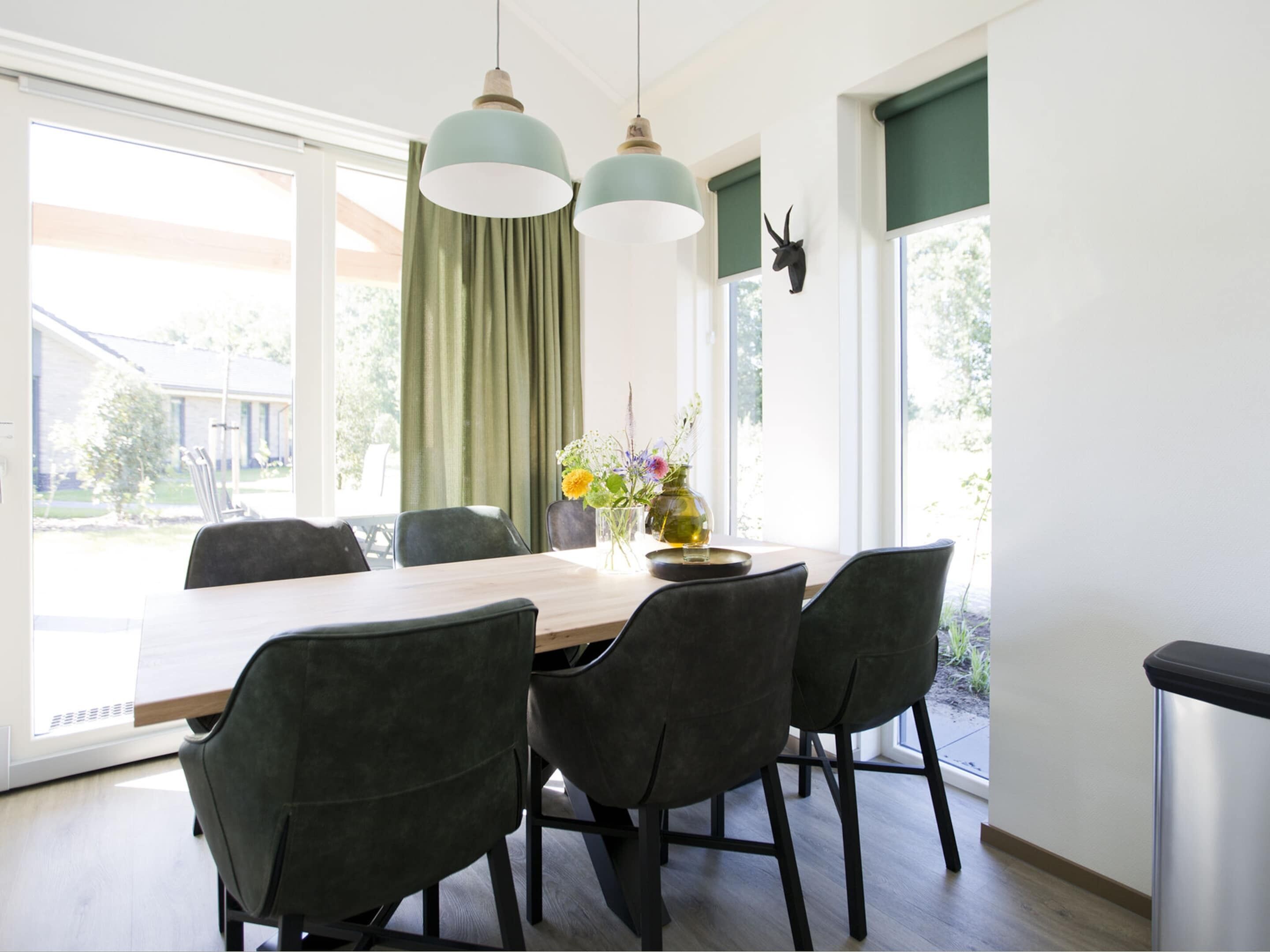 A dining area with a wooden table, four chairs, two pendant lights, and a vase with flowers.