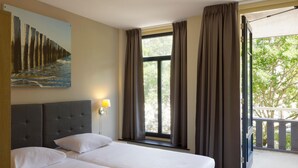 Une chambre d’hôtel avec deux lits, une grande fenêtre avec des rideaux, un tableau représentant une jetée et un balcon avec une balustrade.