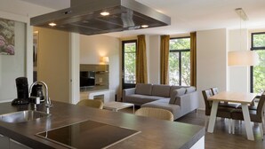 Une cuisine moderne dotée d’une cuisinière intégrée, un coin repas avec une table et des chaises, un canapé et un téléviseur en arrière-plan.