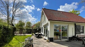 A house with a tiled roof, a patio with a table and chairs, and a garden area. - Spacious Home with Garden near Langweerder Wielen (Sint Nicolaasga)