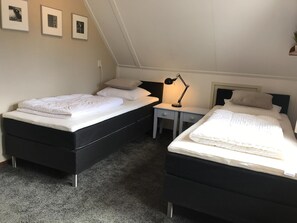 Una habitación con dos camas, un escritorio, una lámpara y cuadros enmarcados en la pared.