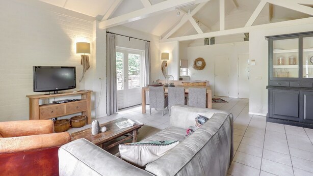 A spacious living area with a television, sofa, and dining table. - Villa in Sandberghe With Sauna and Comfort (Uden)