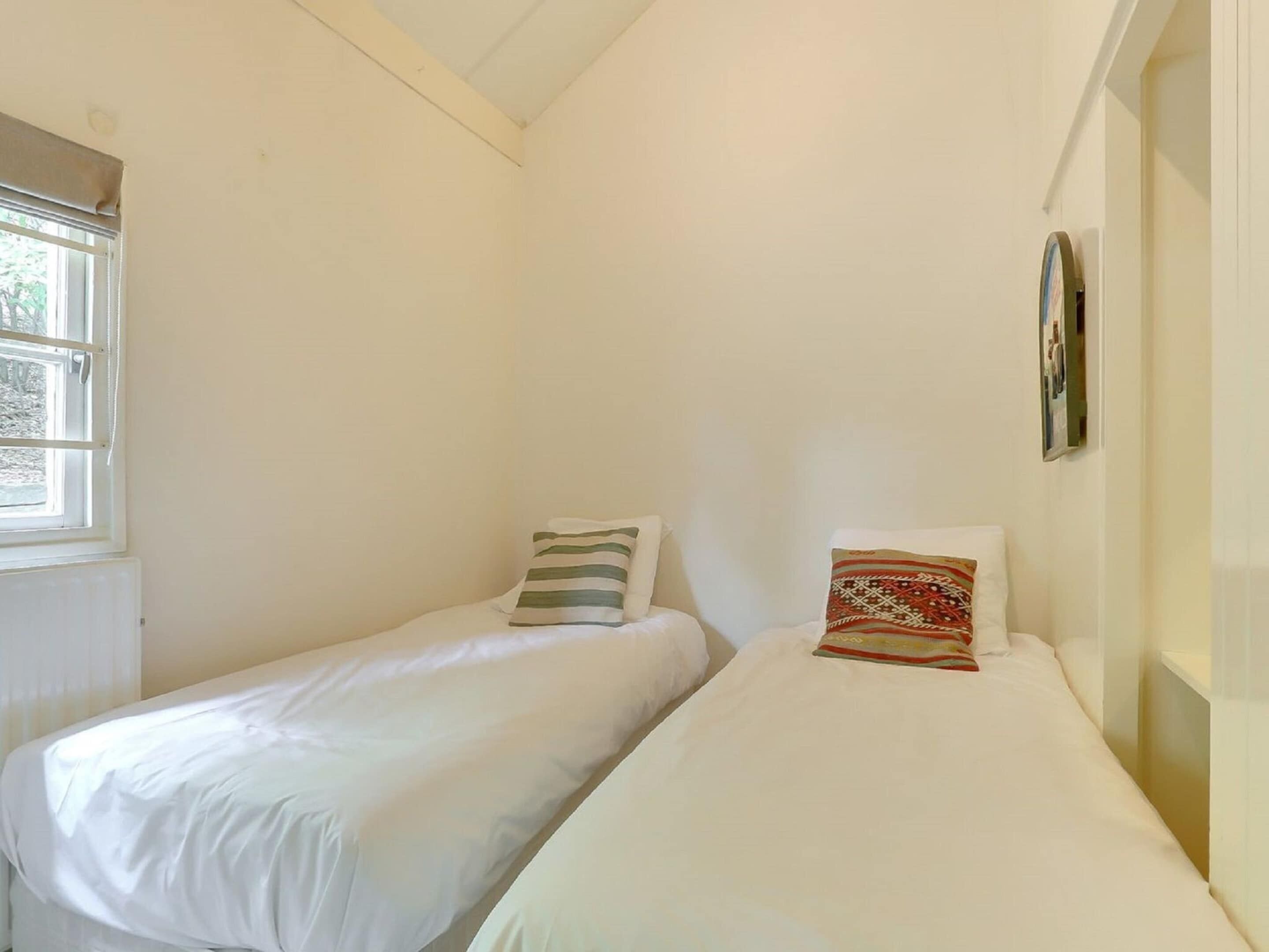 A small, single-room accommodation with two single beds, a window, and a wall-mounted picture.