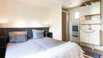 A bedroom with a bed, bedside tables, a mirror, and a bathroom with a sink and towel rack.