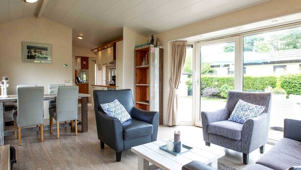 Ein modernes Wohnzimmer mit Essbereich, einer Küche im Hintergrund und großen Schiebeglasüren zum Garten.
