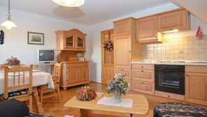 Uma sala de estar acolhedora com uma mesa de jantar de madeira, um sofá e uma televisão. A cozinha possui armários de madeira e um fogão.
