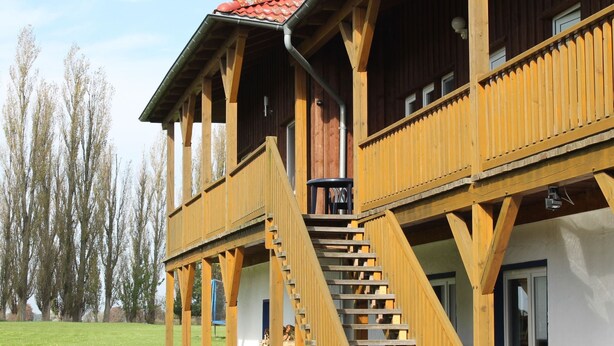 A wooden building with a balcony, a staircase, and a pile of firewood outside. - Expansive Holiday Home in Mecklenburg near Baltic Sea (Walkendorf)