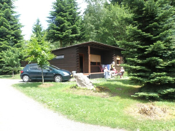 A small log cabin with a porch, a car parked in front, and a grassy area with trees. - Tidy Furnished Wooden Chalet near Forest (Buchet)