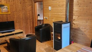 A wooden-paneled room with a TV, two black leather sofas, a wooden table, and a black wood stove.